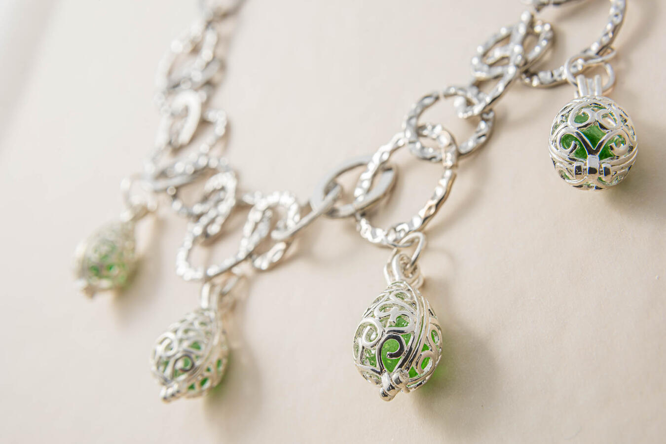 A handcrafted silver chain necklace featuring four ornate filigree cage pendants, each containing a piece of vibrant, translucent green sea glass.