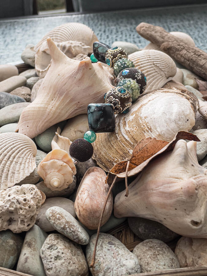 A unique artisan bracelet featuring earth-toned and turquoise beads nestled among a collection of natural conch shells and sea stones.